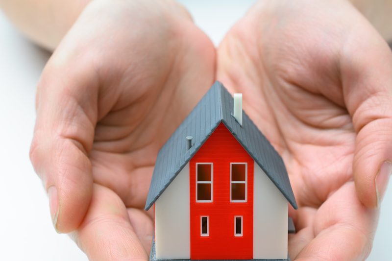 Zwei Hände halten ein kleines Modellhaus mit rotem Giebel
