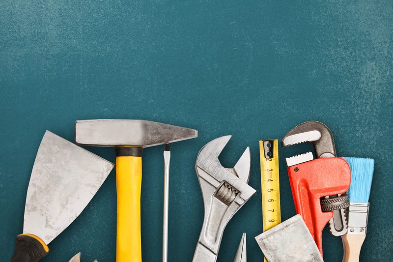 Hammer, Zangen, Zollstock und Pinsel auf dunklem Untergrund